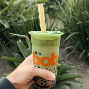 A HAY! Boba tea Straw in a matcha, green milk tea with black tapioca balls. the drink is being held by a male hand.