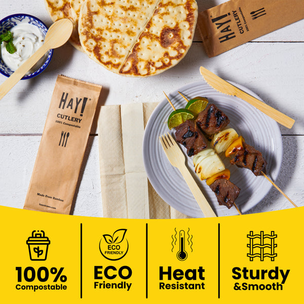 Hay! Cutlery set with a plate of food and skewers on a wooden surface and key benefits of this wooden utensil set like 100% compostable, eco friendly, heat resistant and smooth and sturdy