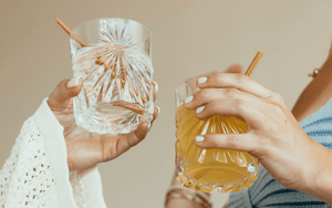 HAY! Straws in a cocktail glass being held by two women saying cheers