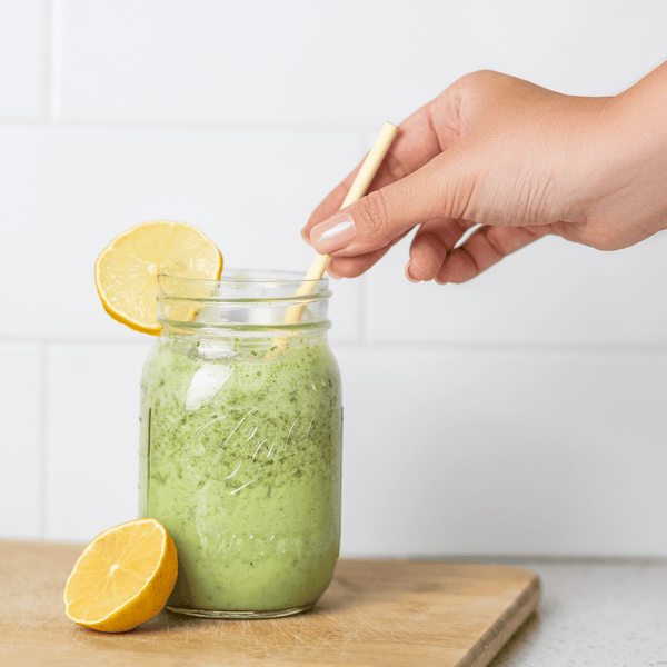 HAY Straws Jumbo Slim Straws made from reed plant stems, a biodegradable smoothie straw,  green smoothie with a natural straw and a woman's hand reaching for the straw, 8” length, non soggy straws, compostable straws, natural straws