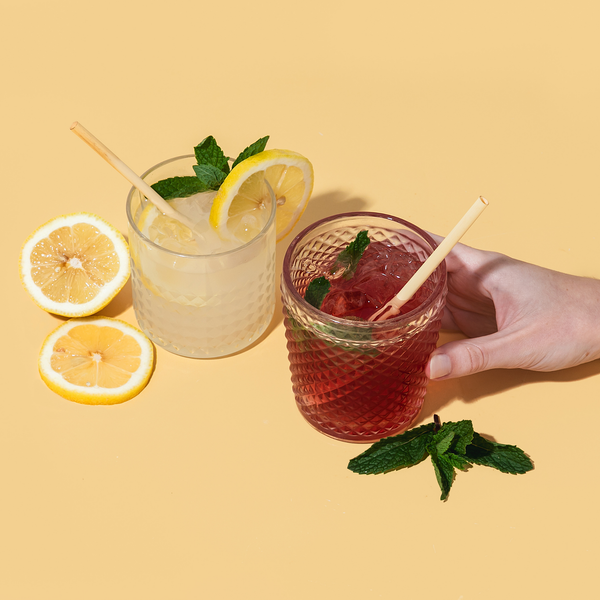 Two glasses of lemonade with mint leaves on a yellow background featuring HAY! Straws martini size 6" straws in a low ball cocktail glass